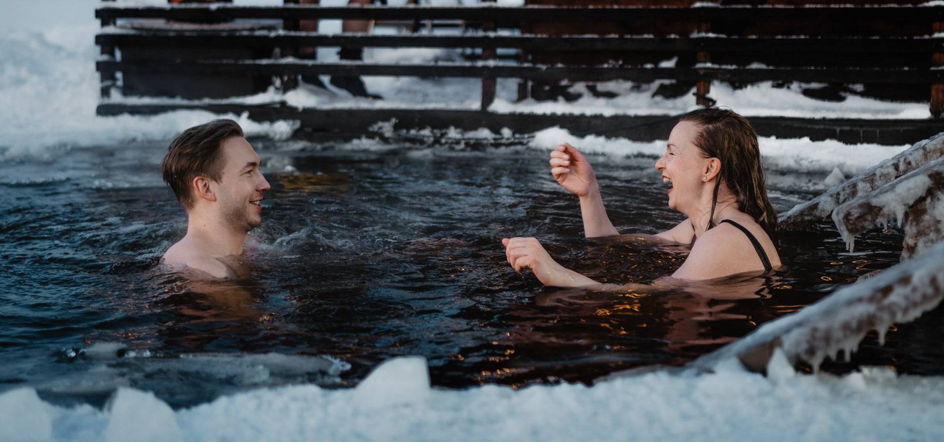 A man and a woman swimming in frozen Ounasjoki river and laughing to each other