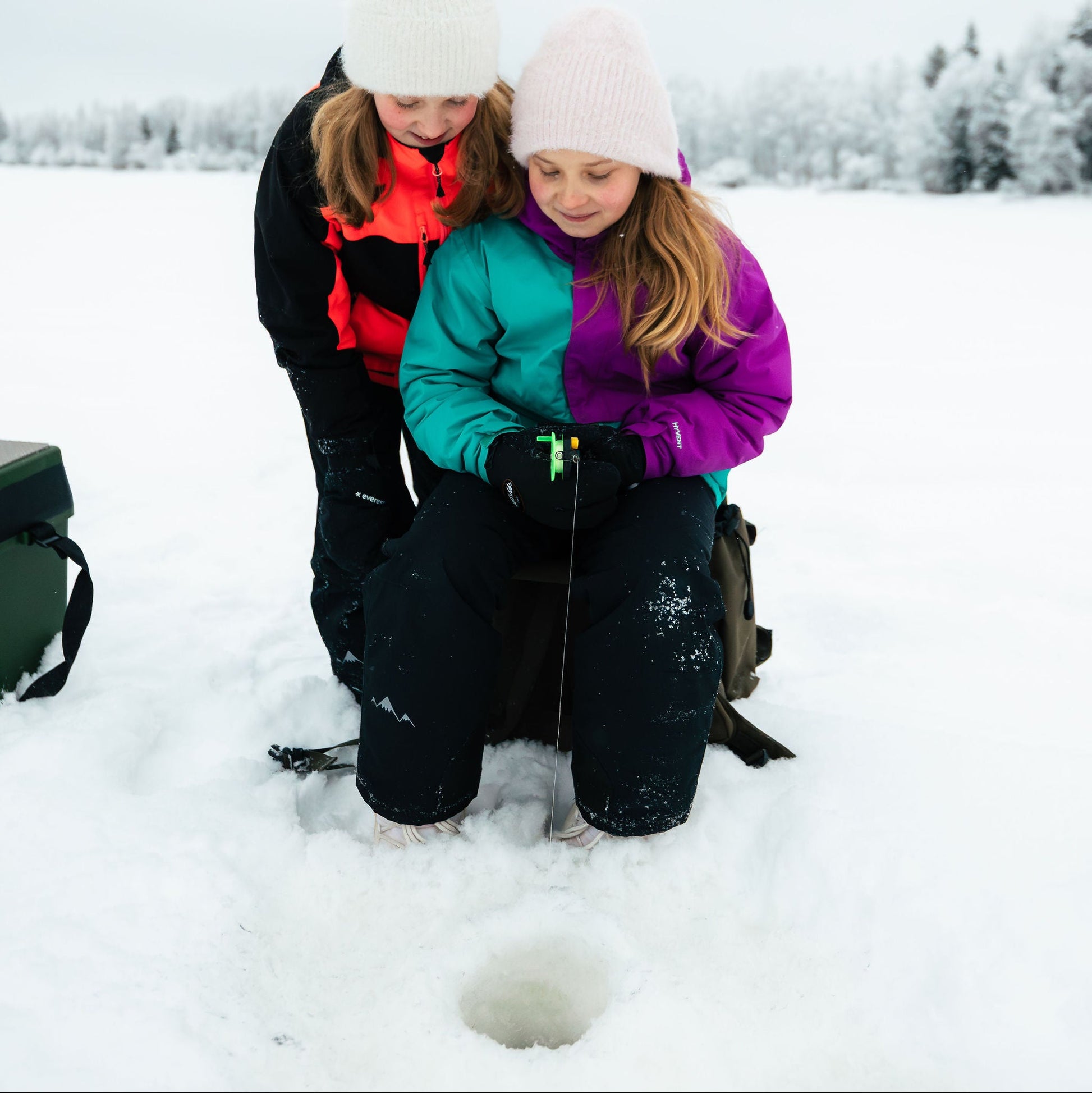 Two children ice fishing in a snowy landscape