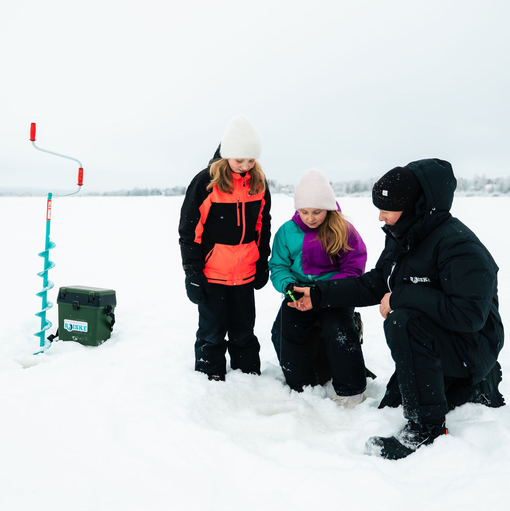 Three people ice fishing in a snowy landscape with a portable ice fishing hole.