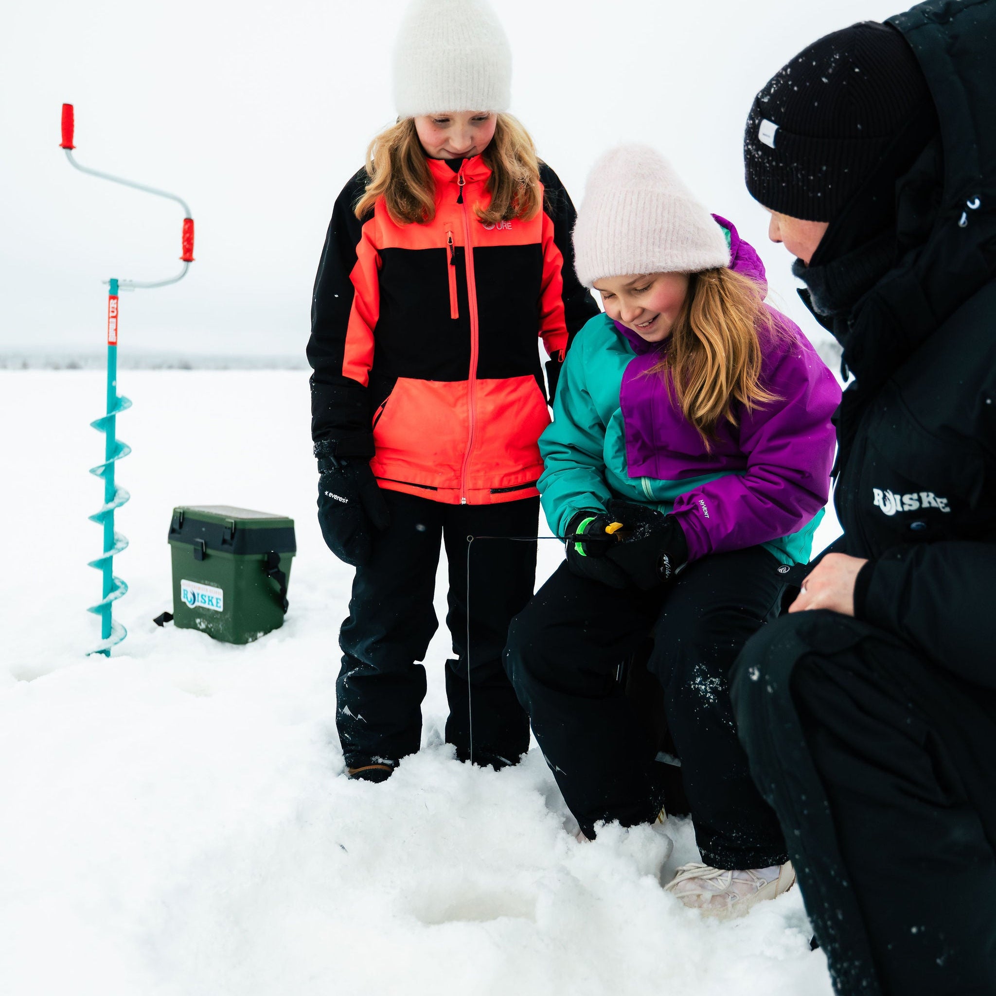 Three people ice fishing in a snowy landscape with a fishing hole and equipment.