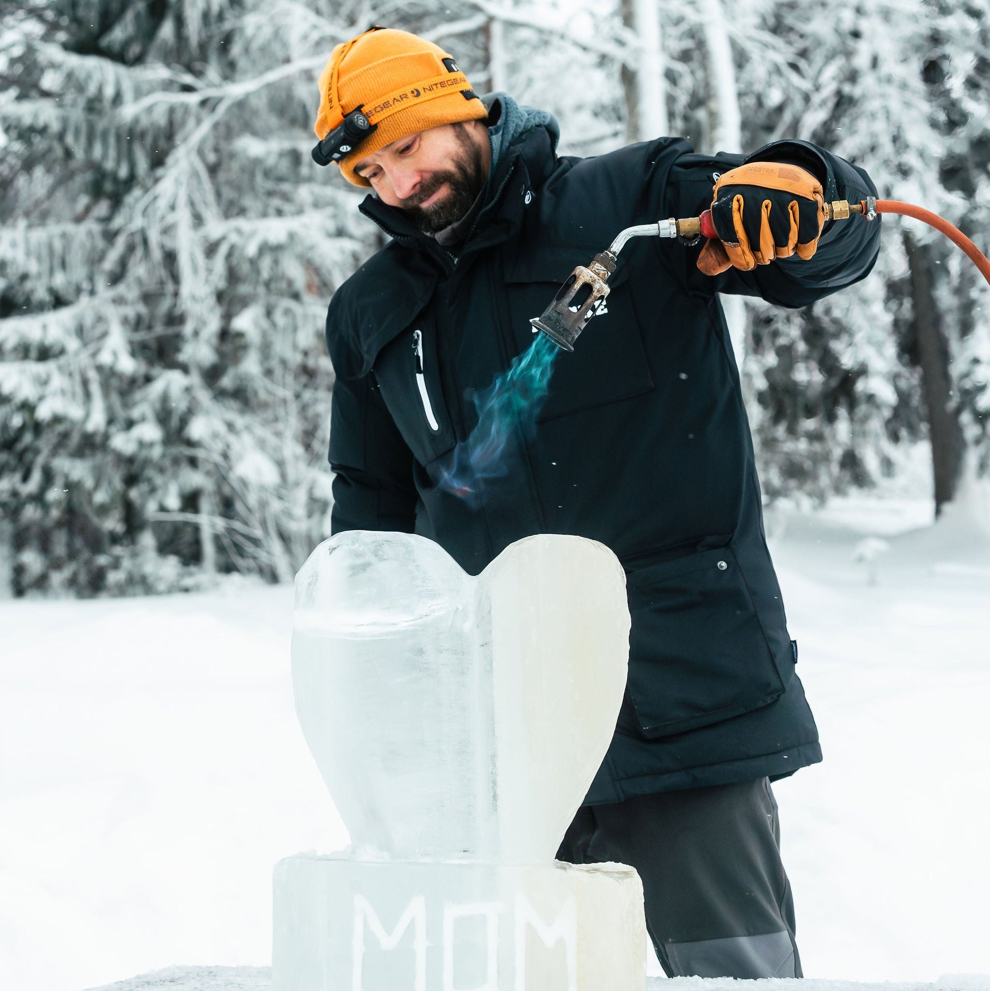 Person using a torch to work on an ice sculpture in a snowy forest.