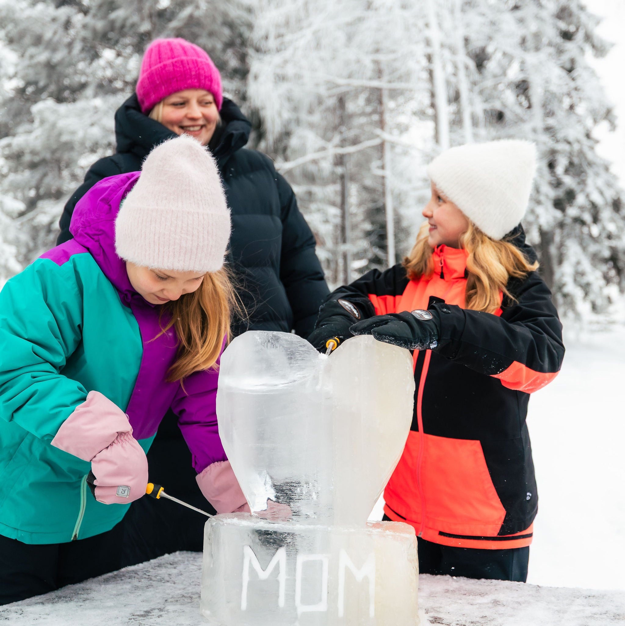 Three people working on an ice sculpture with 'MOM' engraved in the snow.