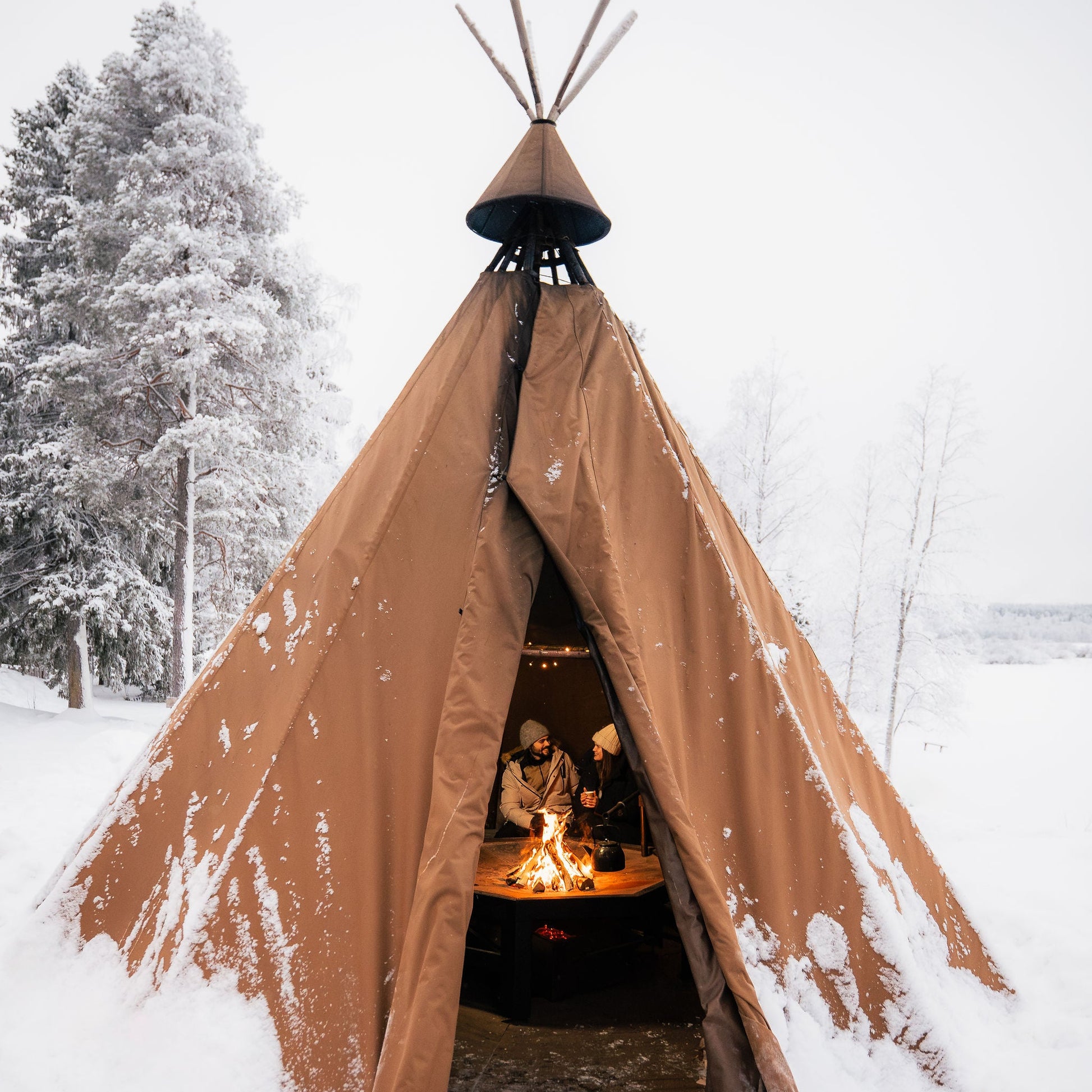 Brown teepee in a snowy landscape with people inside.