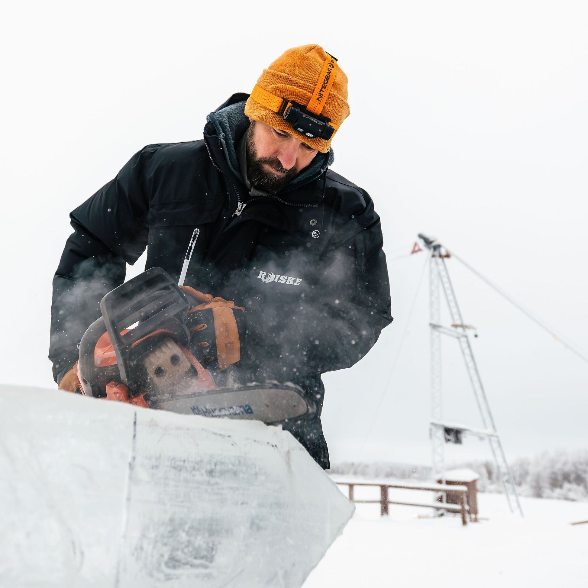 Person using a chainsaw to cut ice in a snowy landscape