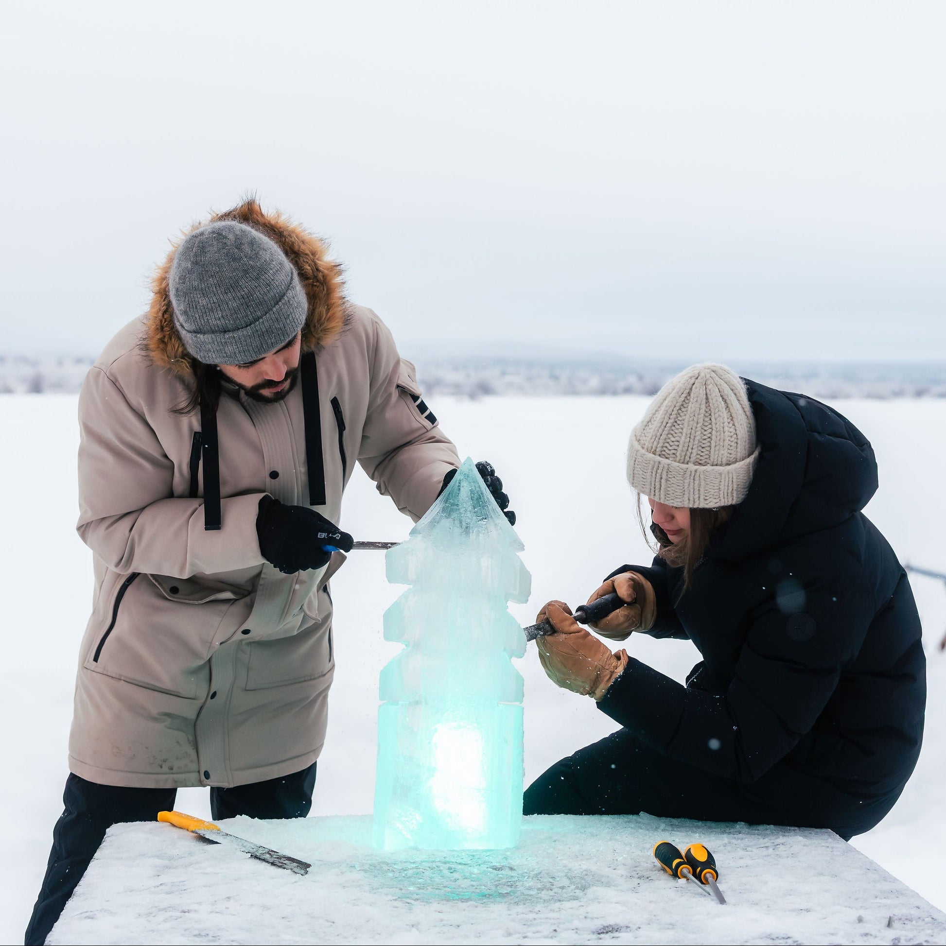 Two people working on an ice sculpture in a snowy landscape