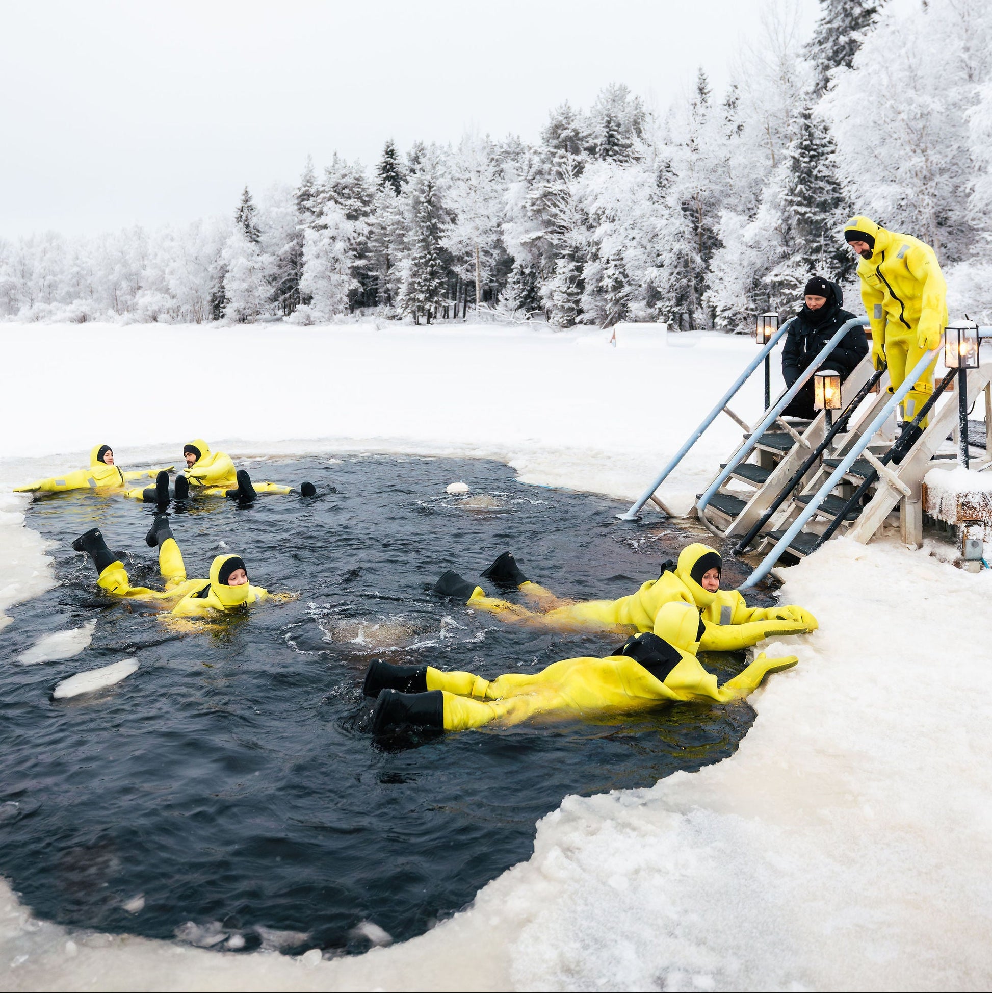People in yellow wetsuits participating in ice swimming in a snowy landscape.