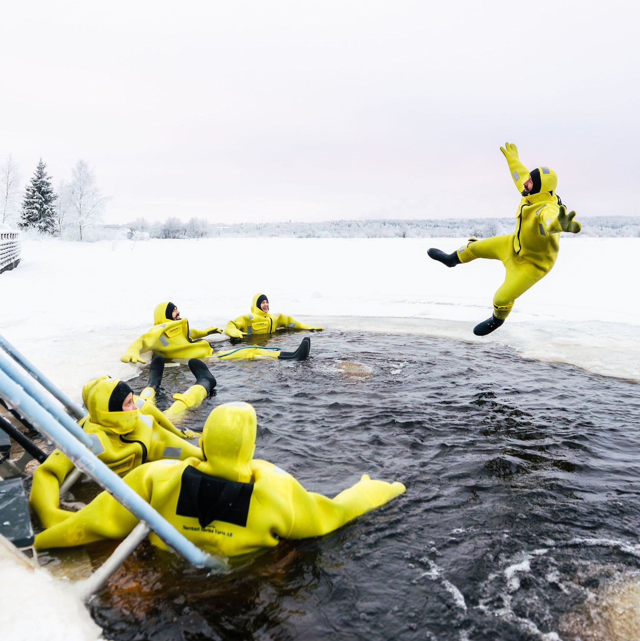 People in yellow suits on a frozen lake with one person jumping into the water.