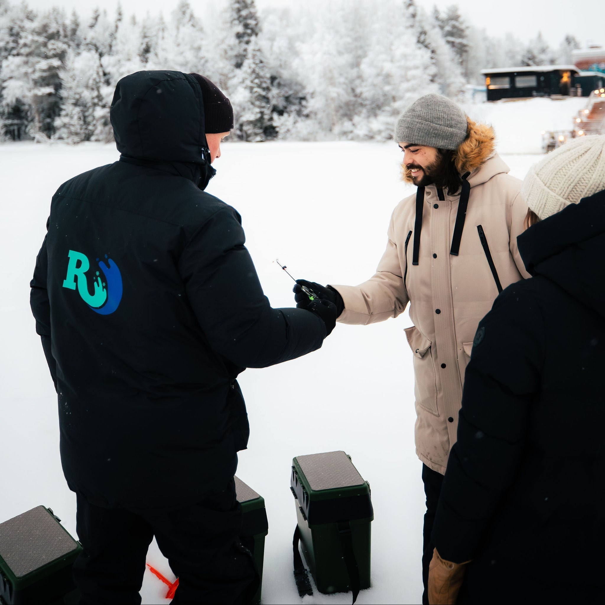 Two people in winter clothing standing on a snow-covered ground with trees in the background.