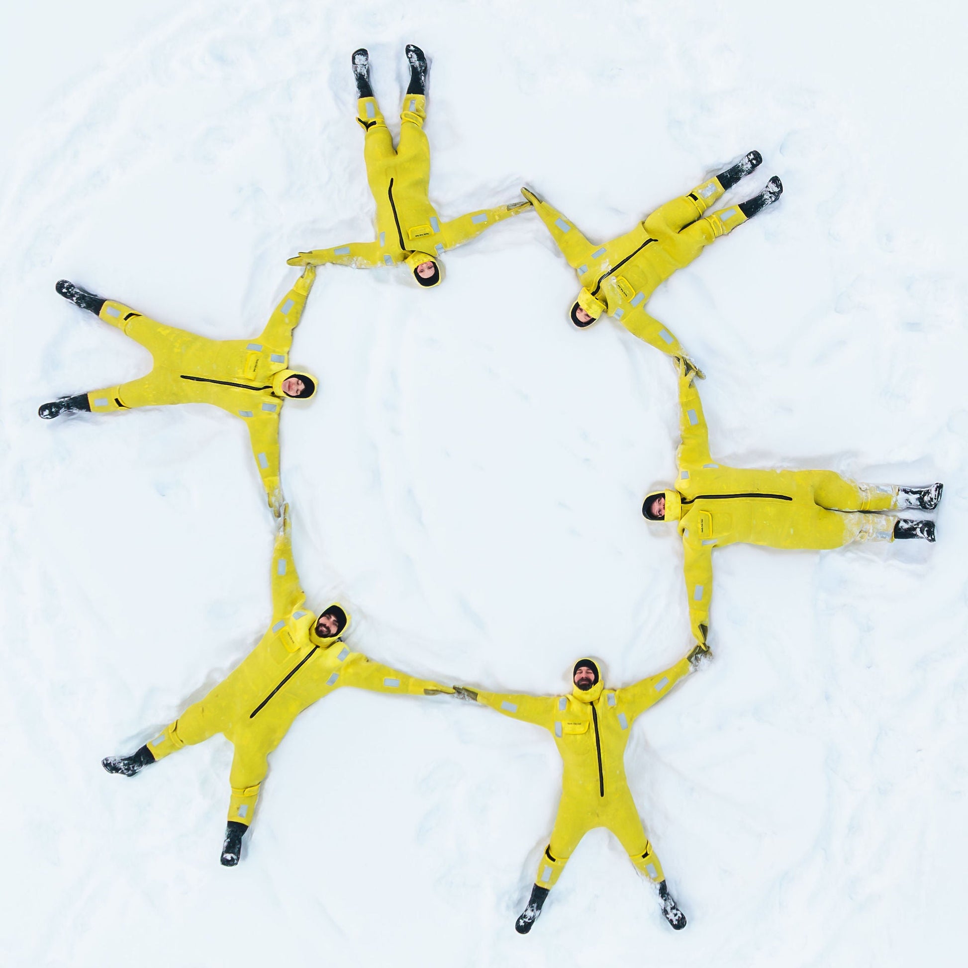 Multiple people in yellow snowmobile suits arranged in a circle on a snowy background