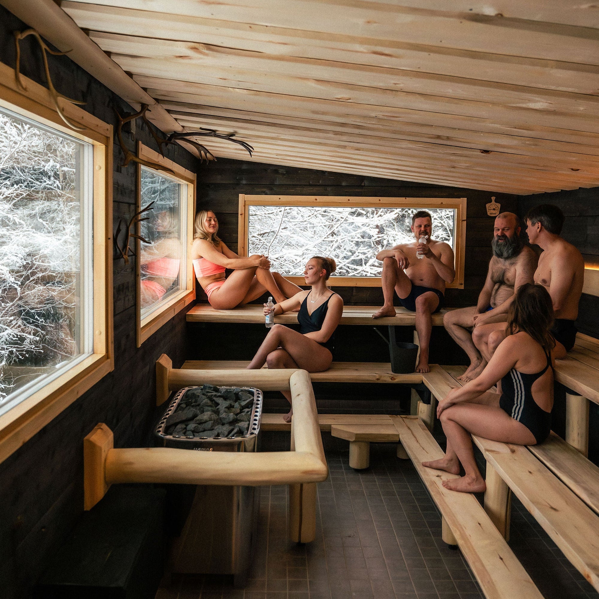 People relaxing in a wooden sauna with large windows.