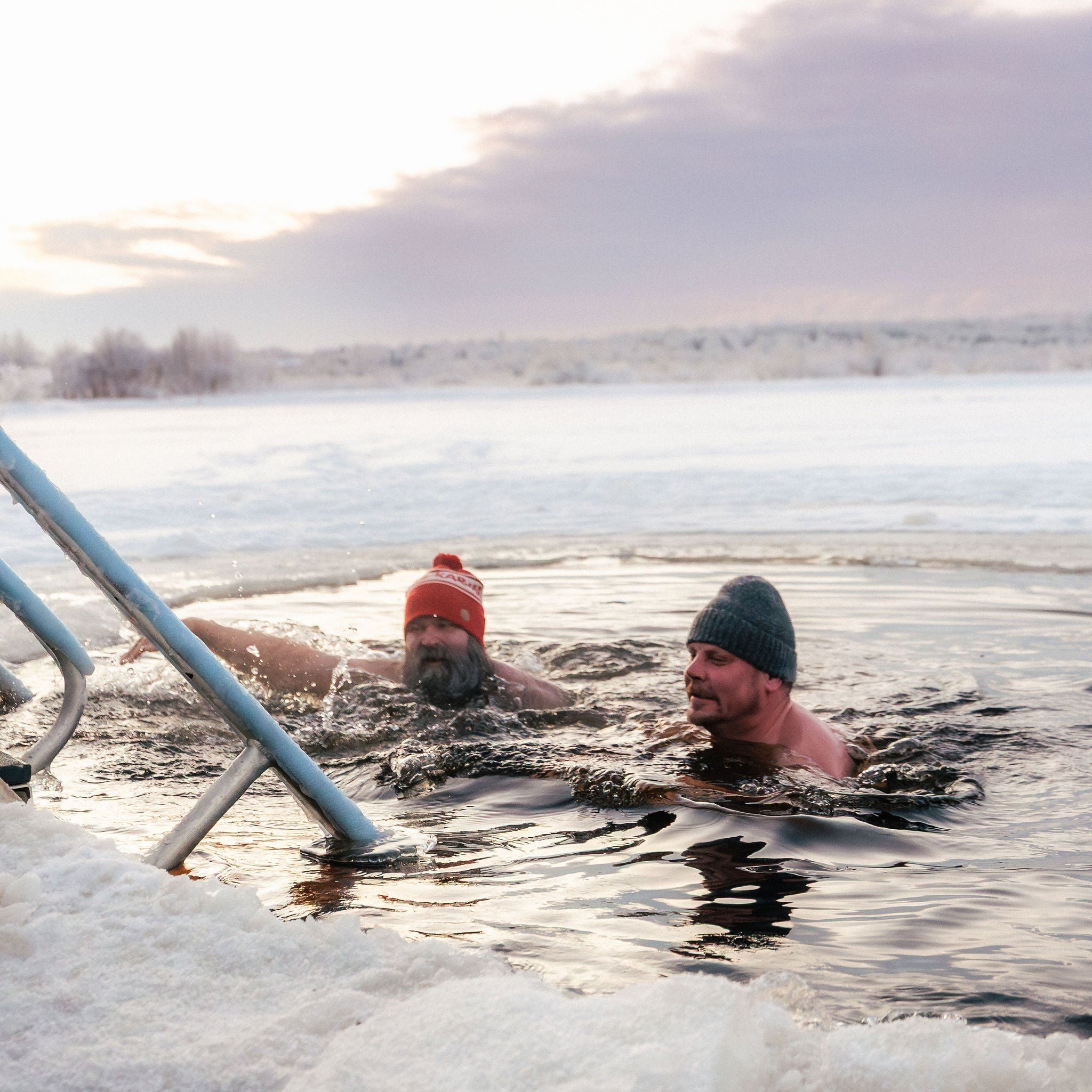 Two people swimming in a cold body of water with a scenic background