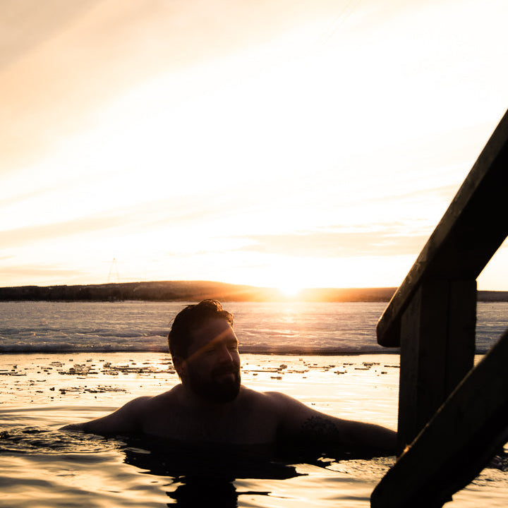 Man swimming in an ice hole at Roiske Arctic Sauna Retreat during spring time