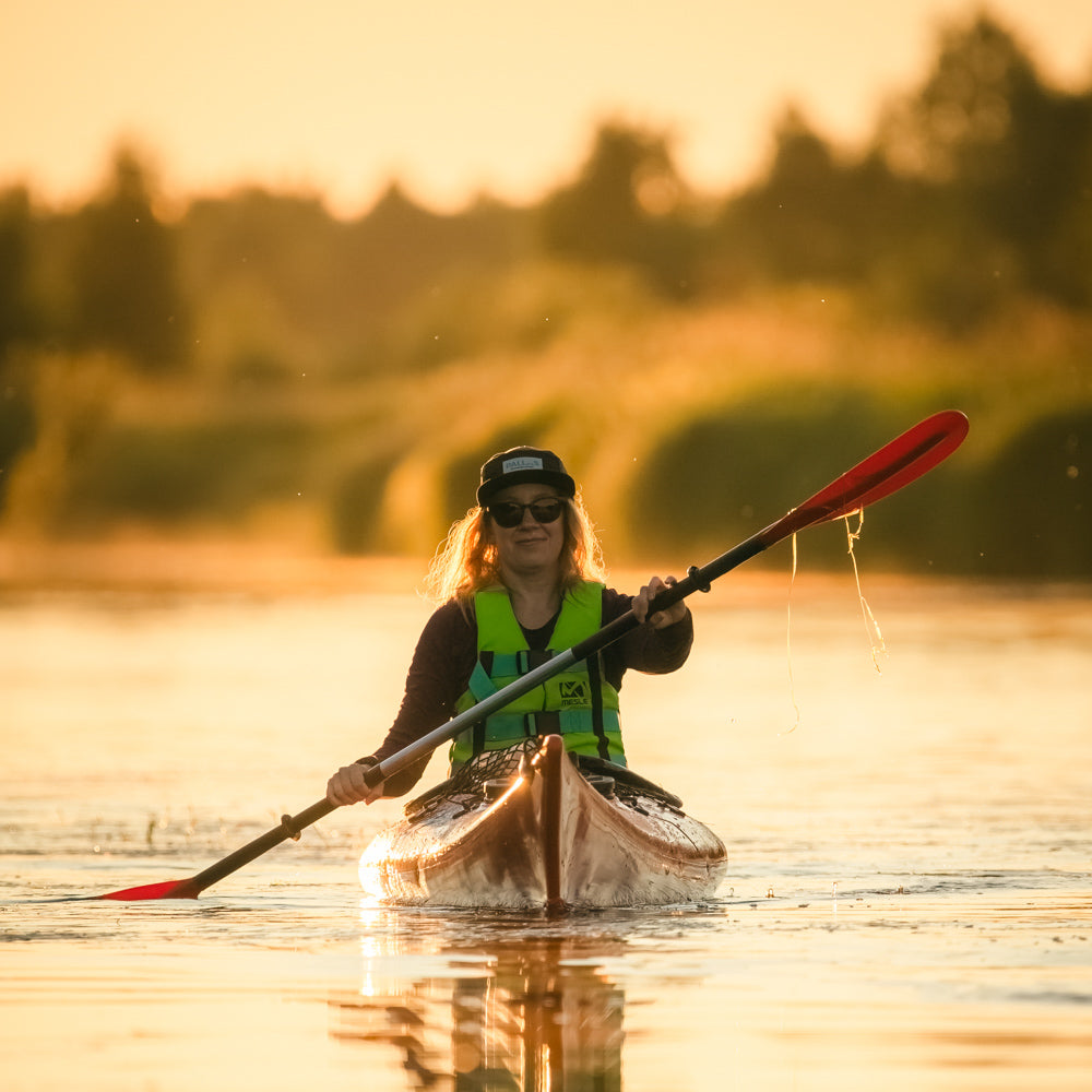 A woman kayaking through the beautiful scenery of the Ounasjoki River under the midnight sun.