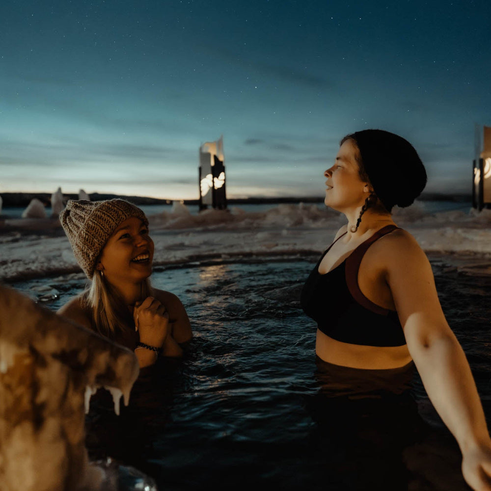 Two women taking a refreshing ice swim at Roiske Arctic Sauna Retreat