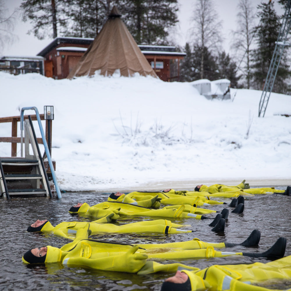 People floating in frozen river with immerion suits at Roiske Arctic Sauna Experience