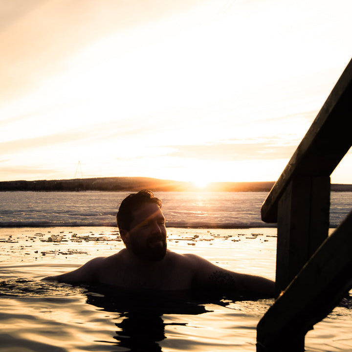 A man is ice swimming during sunset at Roiske Arctic Sauna Retreat