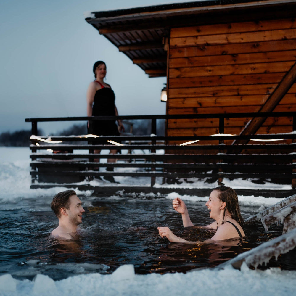 A man and a woman are doing ice swimming and laughing to each other at Roiske Arctic Sauna Retreat