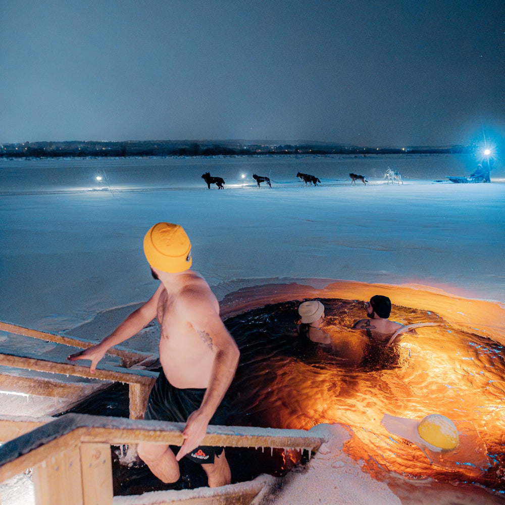 People enjoying ice swimming at Roiske Arctic Sauna Retreat while huskies go by